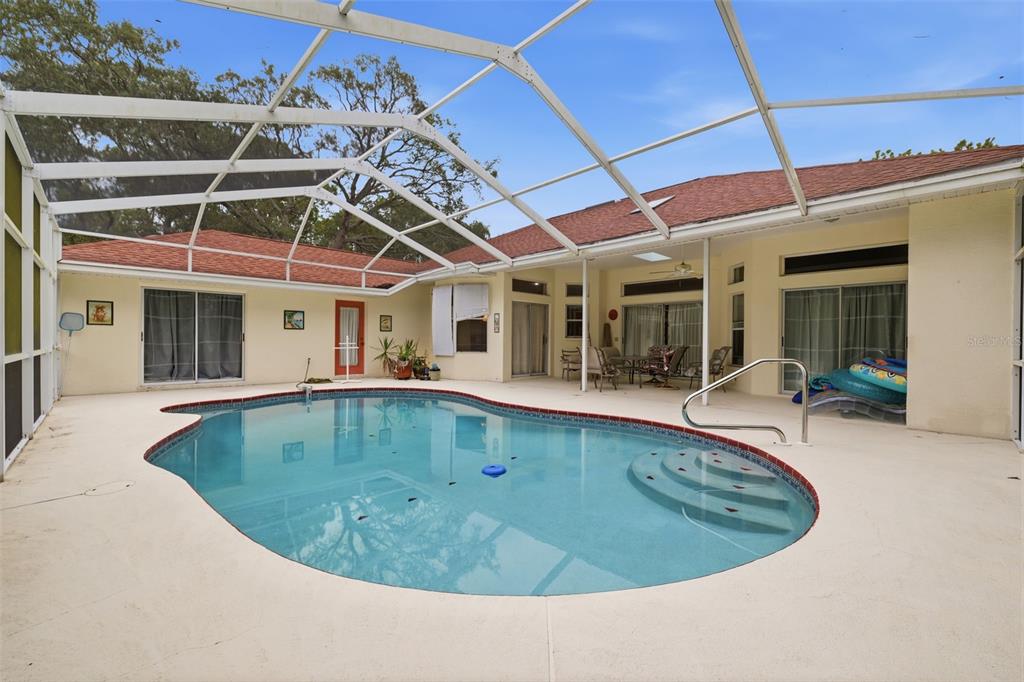 A swimming pool with a screen enclosure sits on a patio next to a house — 184 PINE STREET, HOMOSASSA, FL