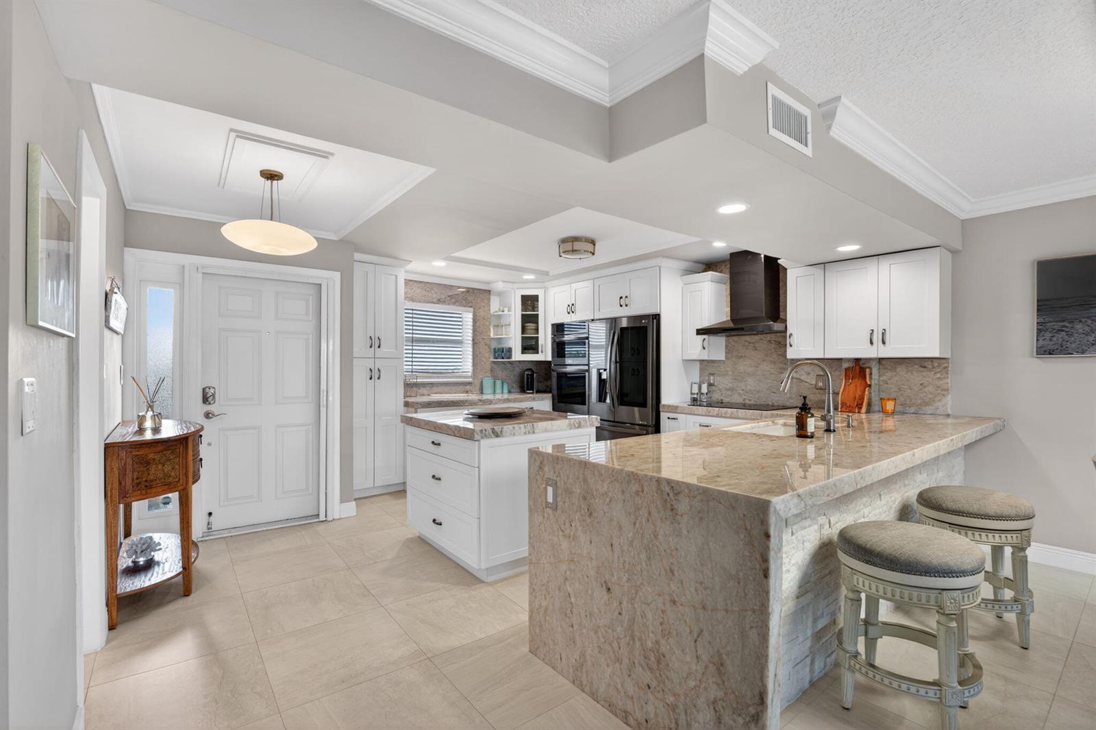 A kitchen features white cabinets, granite countertops, a central island, and a breakfast bar — 1523 E Hillsboro Boulevard # 631, Deerfield Beach FL 33441, DEERFIELD BEACH, FL