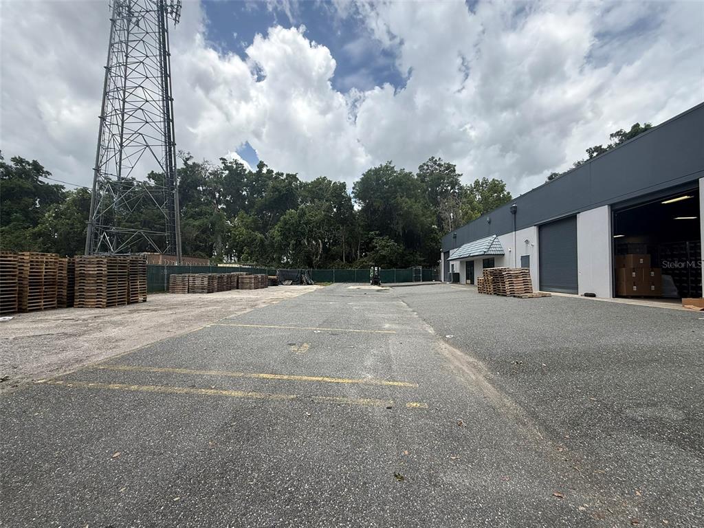 An outdoor industrial area features a paved lot, stacked wooden pallets, and a metal building — 810 NW 25TH AVENUE UNIT 100, OCALA, FL