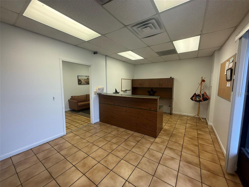 An office reception area features a wooden desk, tiled floors, and a doorway to another room — 810 NW 25TH AVENUE UNIT 100, OCALA, FL