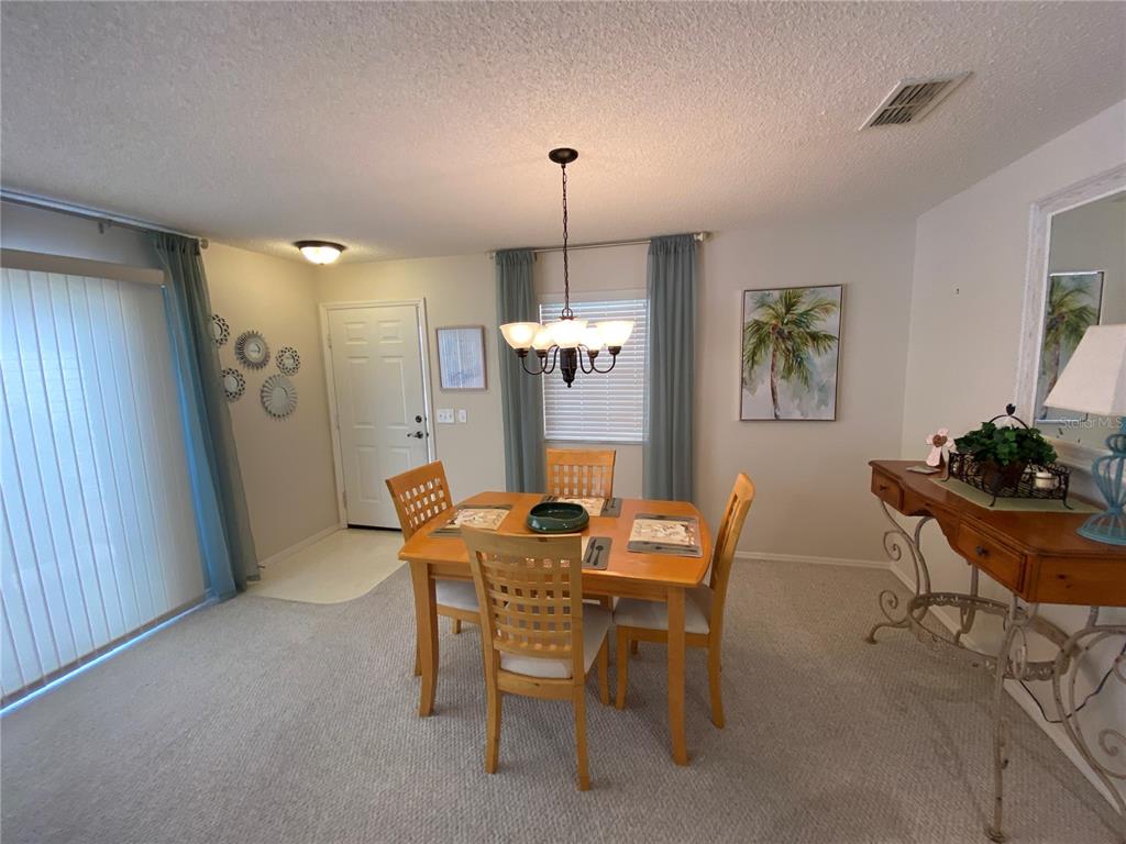 A dining room features a wooden table with four chairs, a chandelier, and carpeted flooring — 1672 DURAN DRIVE, THE VILLAGES, FL