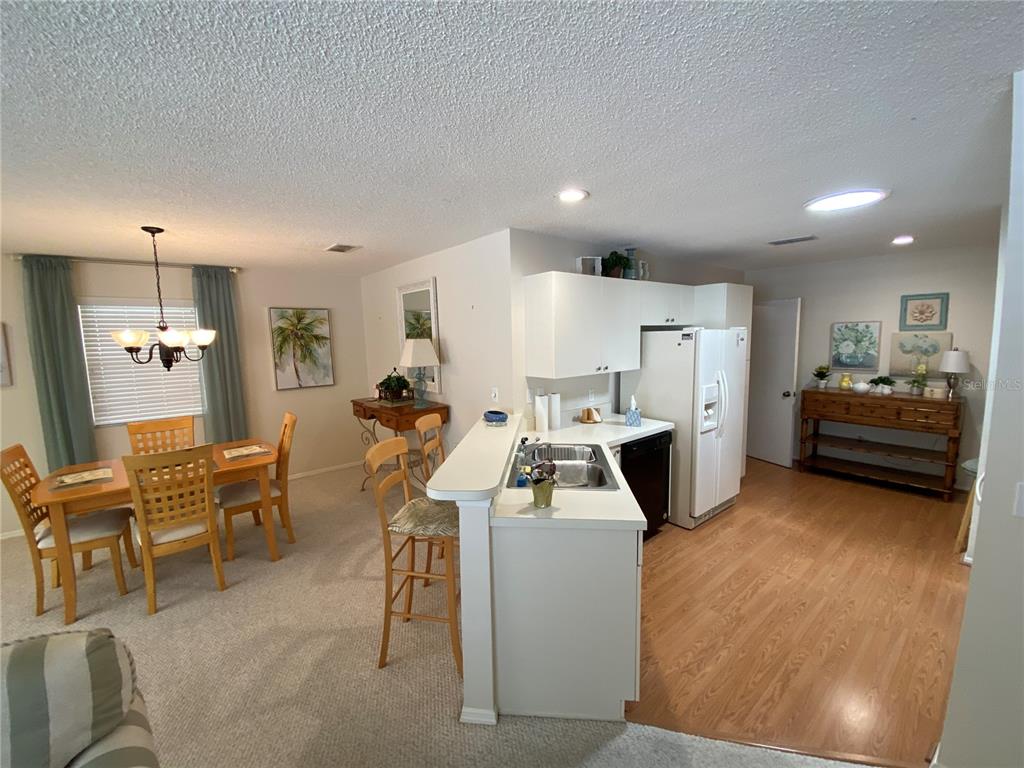 An open-concept kitchen with white cabinets and appliances overlooks a dining area with carpeted floors — 1672 DURAN DRIVE, THE VILLAGES, FL