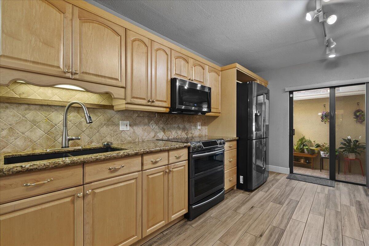 A kitchen with light wood cabinets, granite countertops, black appliances, and wood-look tile flooring — 605 Maplewood Drive, FL 33415, FL