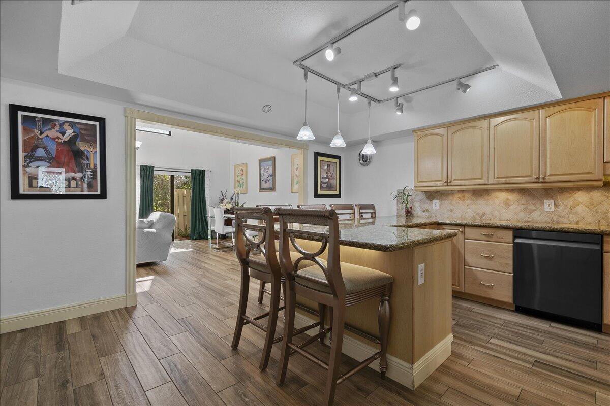 A kitchen with wood cabinets, granite countertops, and a breakfast bar with two stools — 605 Maplewood Drive, FL 33415, FL