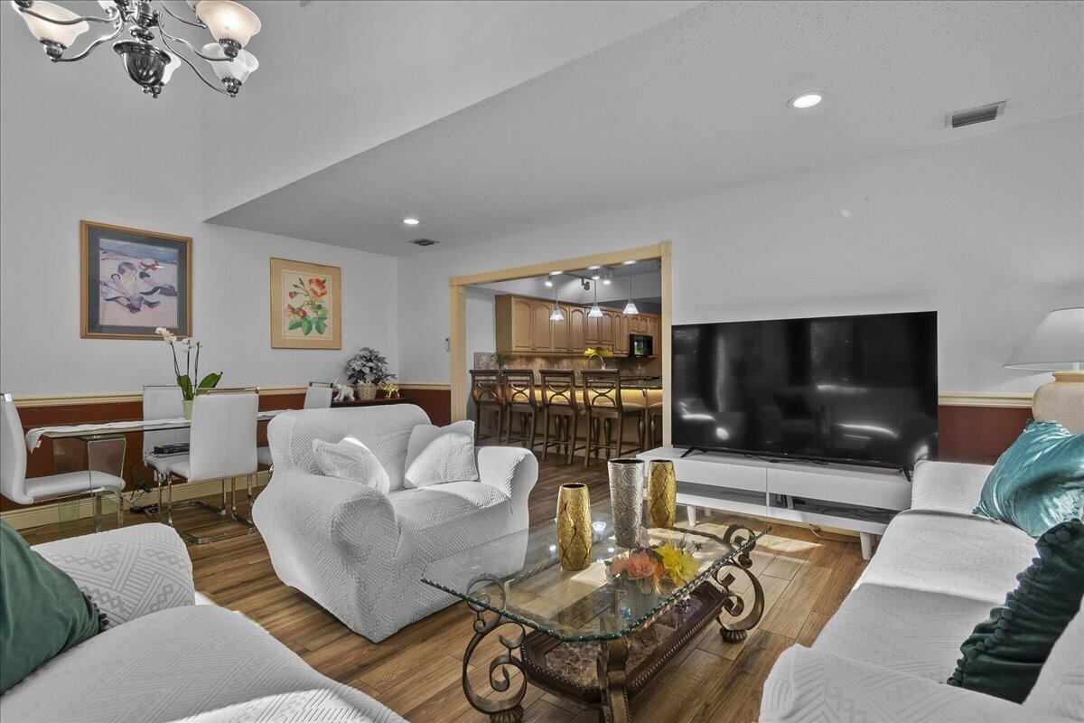 A living room with white slipcovered furniture, a glass coffee table, and an open kitchen — 605 Maplewood Drive, FL 33415, FL