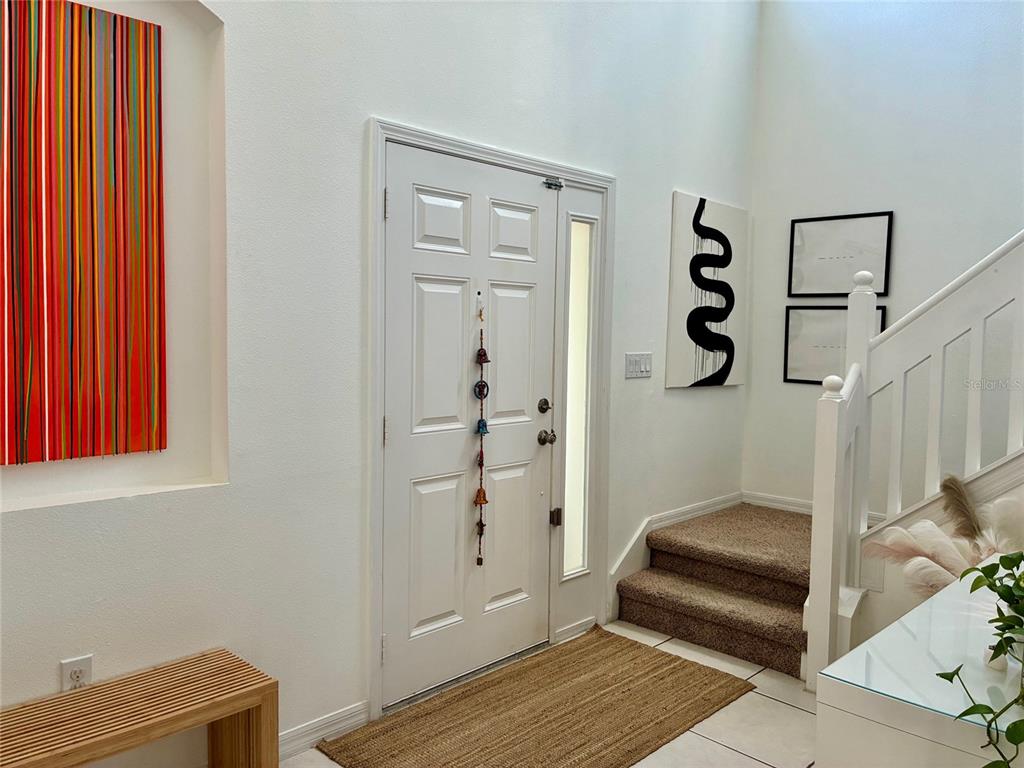A bright entryway features a white front door, a staircase with carpet, and colorful wall art — 8026 CARRIAGE POINTE DRIVE, GIBSONTON, FL