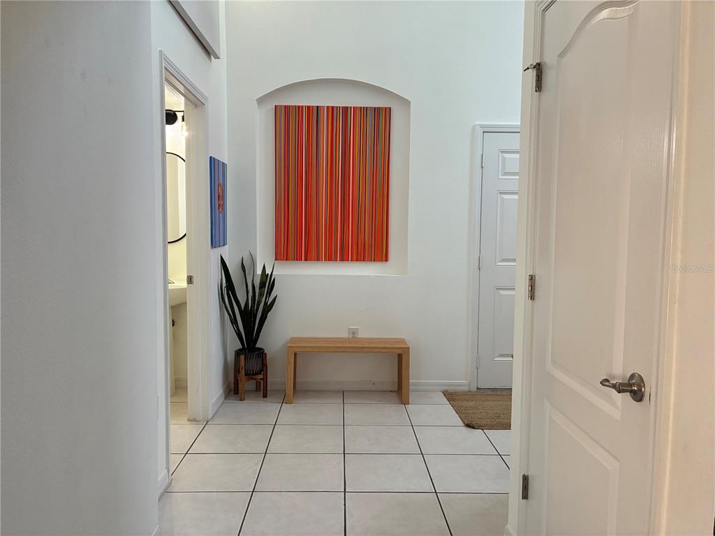 A bright entryway features white tile floors, a wooden bench, and colorful vertical-striped wall art — 8026 CARRIAGE POINTE DRIVE, GIBSONTON, FL
