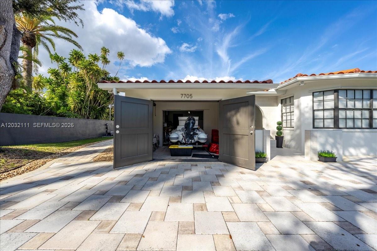 A paved driveway leads to an open garage containing a boat with a motor — 7705 SW 66th St # 0, Miami FL 33143, MIAMI, FL