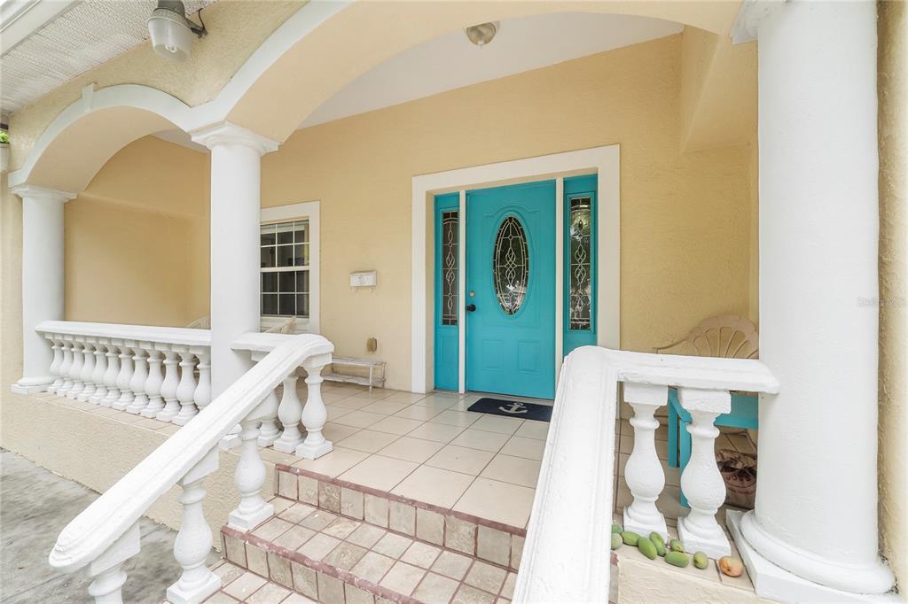 A covered porch features a bright blue front door, white balustrades, and tiled steps — 1701 38TH AVENUE, ST PETERSBURG, FL