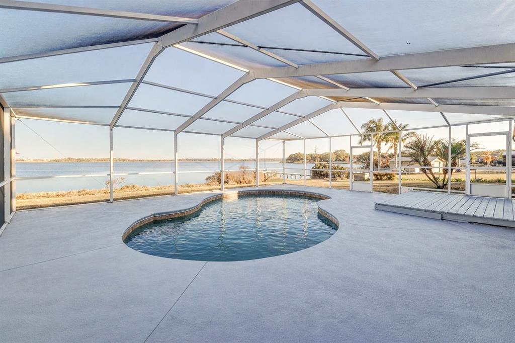 A screened-in pool enclosure overlooks a lake with a concrete deck and a small dock — 411 EDGEWATER DRIVE, POLK CITY, FL