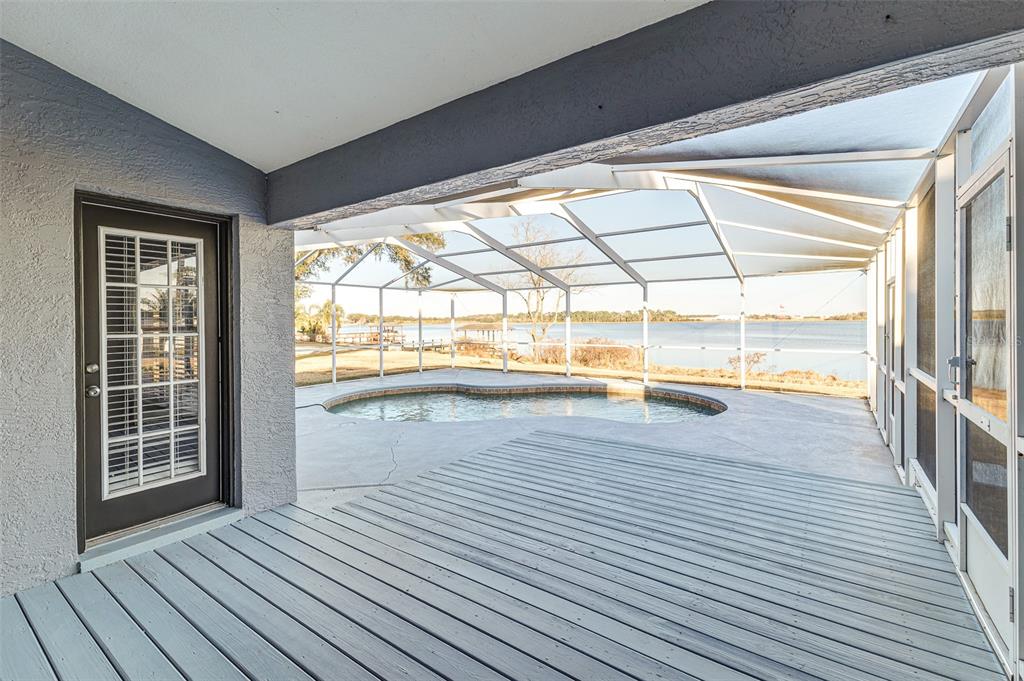 A covered wooden deck overlooks a screened-in pool and a lake in the distance — 411 EDGEWATER DRIVE, POLK CITY, FL