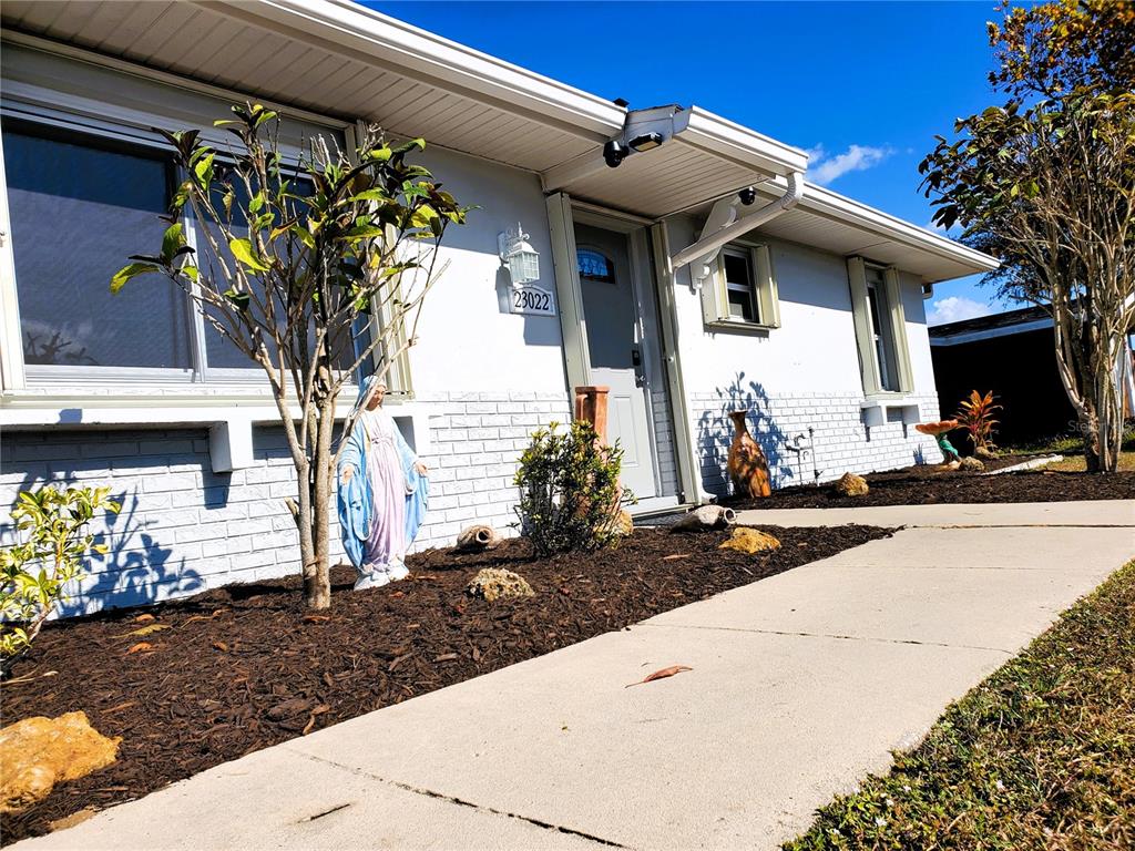A white, single-story house exterior features a front walkway, landscaping, and a statue of Mary — 23022 MCNULTY AVENUE, PORT CHARLOTTE, FL