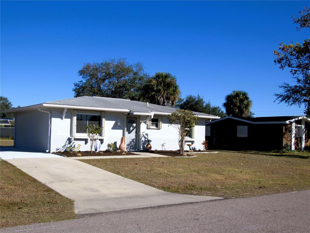 A white, single-story house with a concrete driveway sits under a clear blue sky — 23022 MCNULTY AVENUE, PORT CHARLOTTE, FL