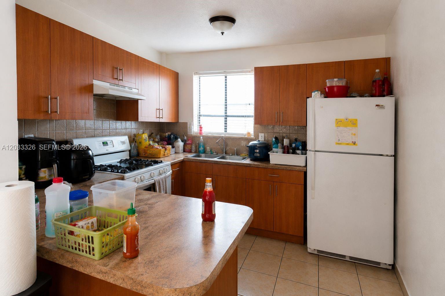 A kitchen features wood cabinets, laminate countertops, a white refrigerator, and a gas range — 6215 W 22nd Ct # 15, Hialeah FL 33016, HIALEAH, FL