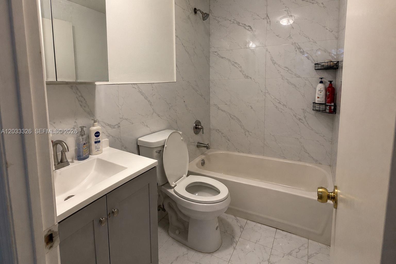 A bathroom features a gray vanity, a white toilet, and a bathtub with marble-patterned tiles — 6215 W 22nd Ct # 15, Hialeah FL 33016, HIALEAH, FL