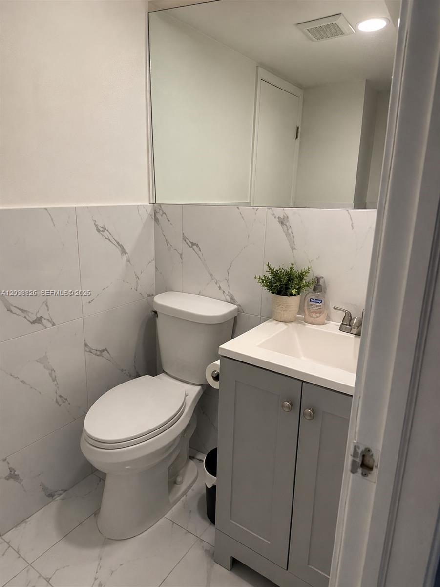 A small bathroom features a white toilet, a gray vanity, and white marble-patterned wall tiles — 6215 W 22nd Ct # 15, Hialeah FL 33016, HIALEAH, FL
