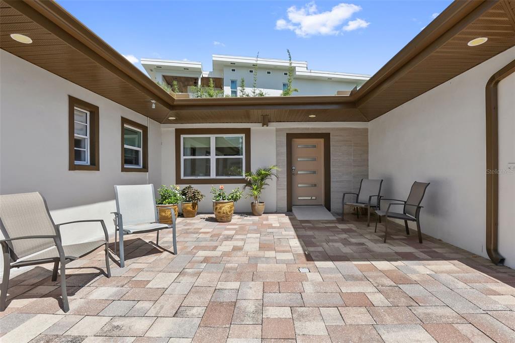 A paved courtyard features four chairs, potted plants, and a front door under an overhang — 25 SANDPIPER ROAD, TAMPA, FL