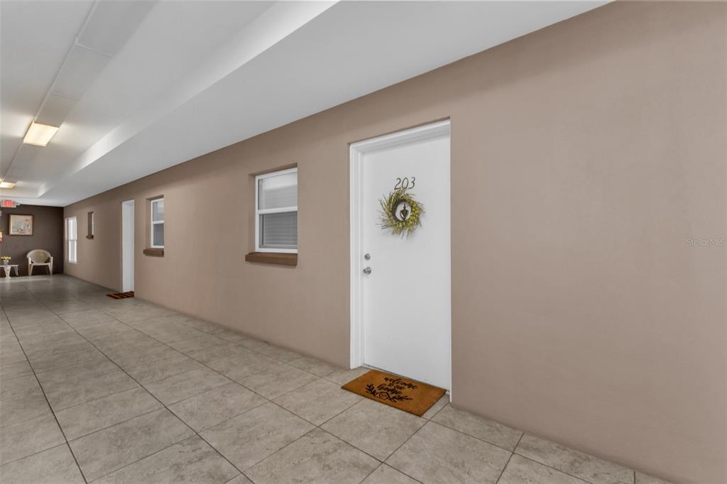 A hallway with tan walls, tiled flooring, and a white door labeled 203 — 3100 HARBOR BOULEVARD UNIT 203, PORT CHARLOTTE, FL