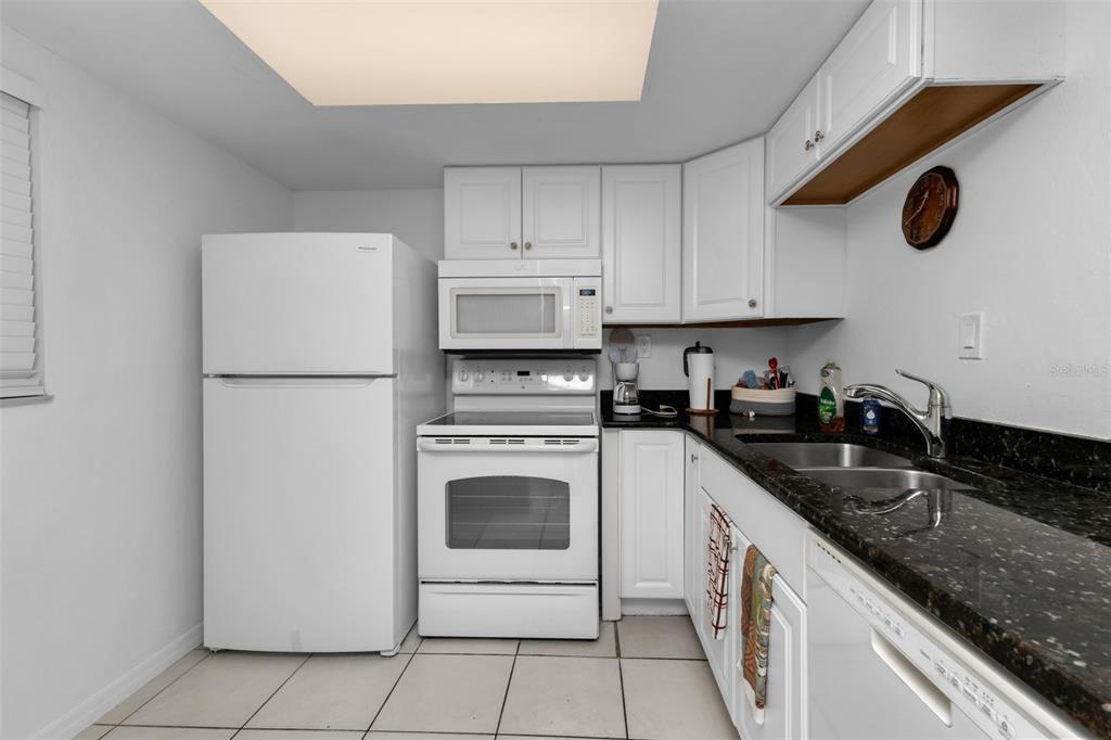 A kitchen features white appliances, white cabinetry, and dark granite countertops with a double sink — 3100 HARBOR BOULEVARD UNIT 203, PORT CHARLOTTE, FL