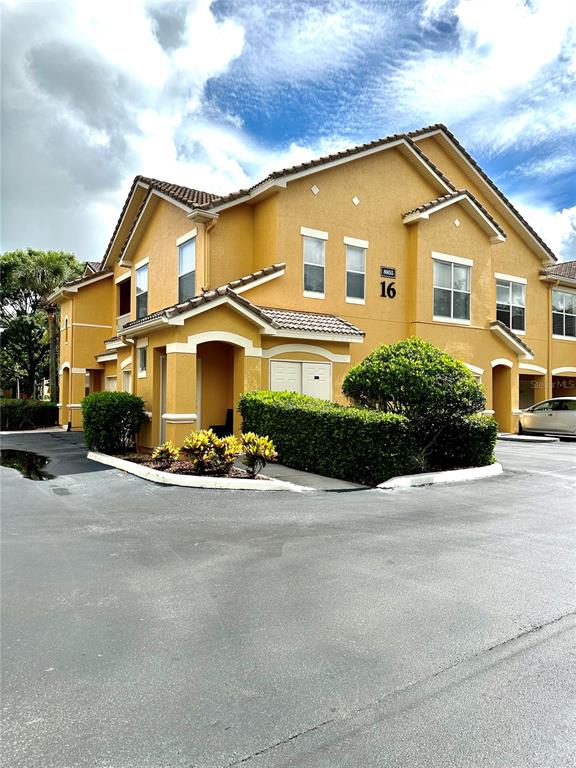 A yellow two-story apartment building features a covered entrance and manicured landscaping — 8855 VILLA VIEW CIRCLE UNIT 105, ORLANDO, FL