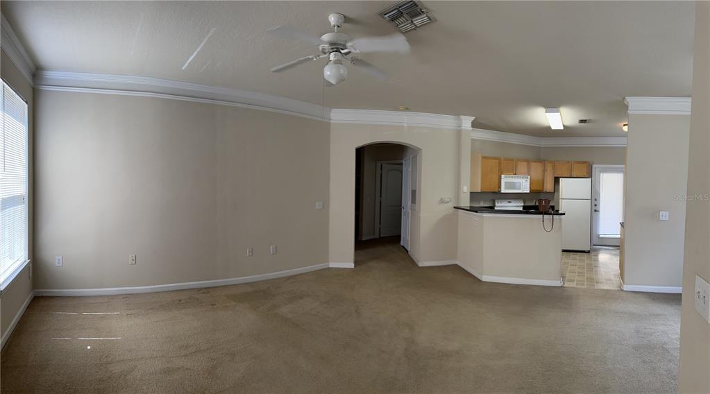 A living room with beige carpet and walls connects to an open kitchen with wooden cabinets — 8855 VILLA VIEW CIRCLE UNIT 105, ORLANDO, FL