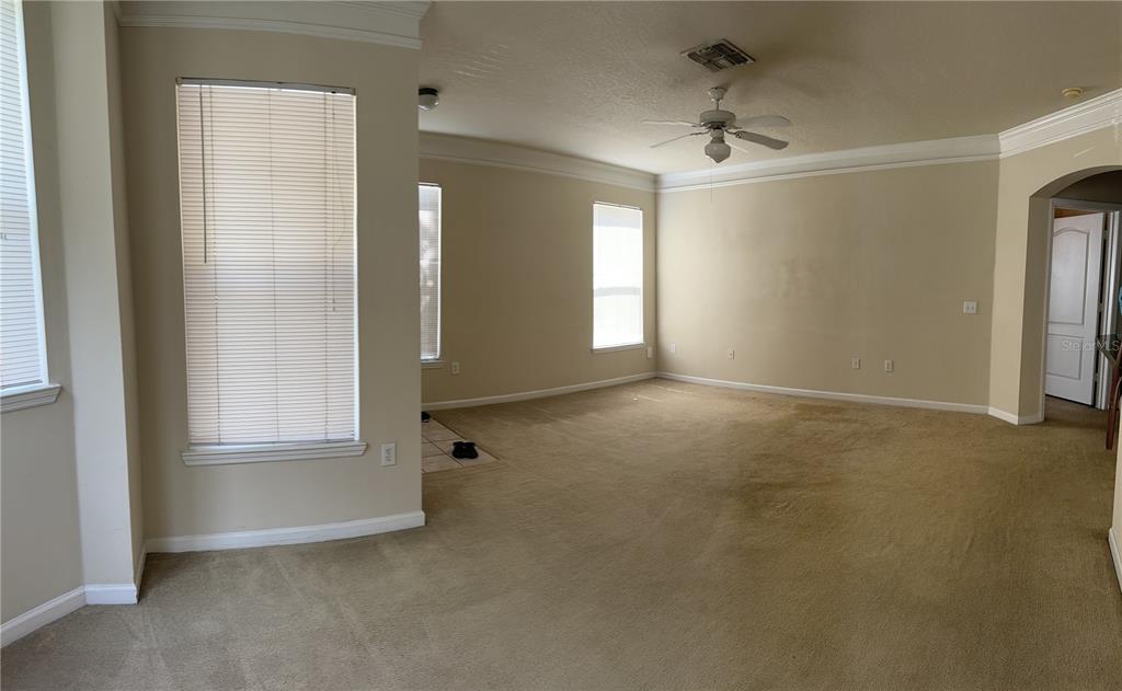 An empty living room features beige carpeting, neutral walls, crown molding, and several windows — 8855 VILLA VIEW CIRCLE UNIT 105, ORLANDO, FL