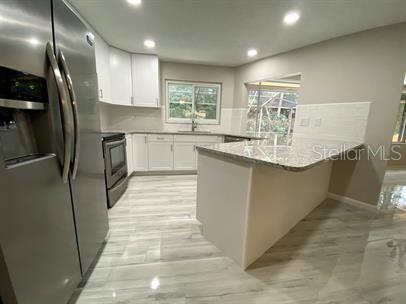 A modern kitchen features white cabinets, granite countertops, stainless steel appliances, and light wood-look flooring — 2 SUNSET BAY DRIVE, BELLEAIR, FL