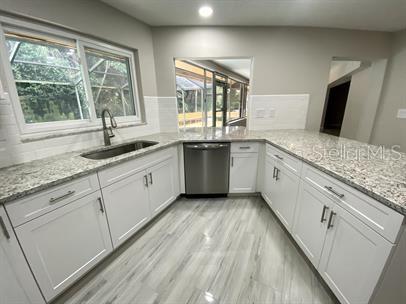 A kitchen features white cabinets, granite countertops, a stainless steel dishwasher, and light-colored tile flooring — 2 SUNSET BAY DRIVE, BELLEAIR, FL