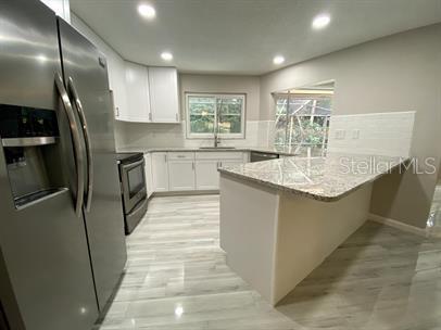 A kitchen features white cabinets, granite countertops, stainless steel appliances, and light wood-look flooring — 2 SUNSET BAY DRIVE, BELLEAIR, FL