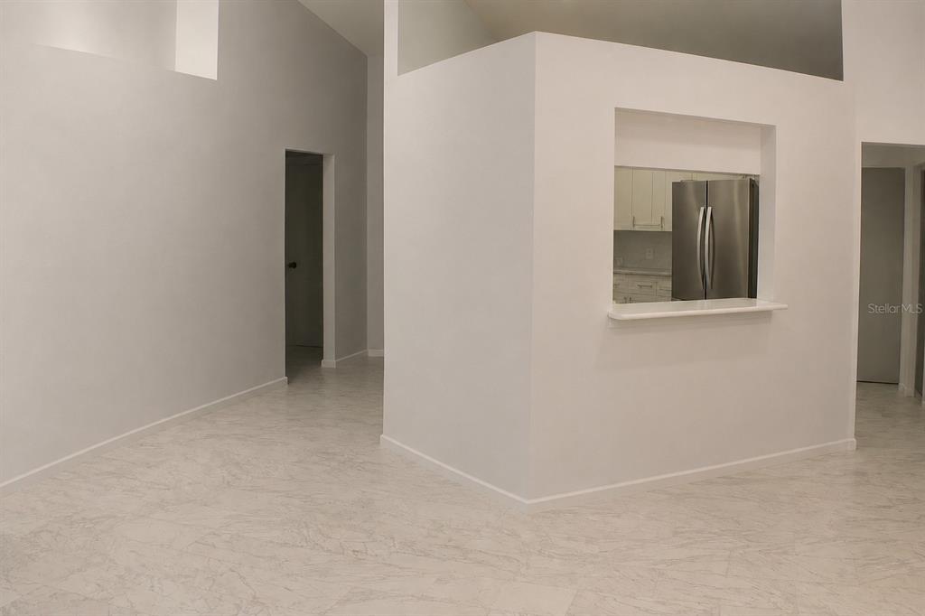 A bright room with white walls, marble-patterned tile flooring, and a kitchen pass-through window — 1723 BELL RANCH STREET, BRANDON, FL