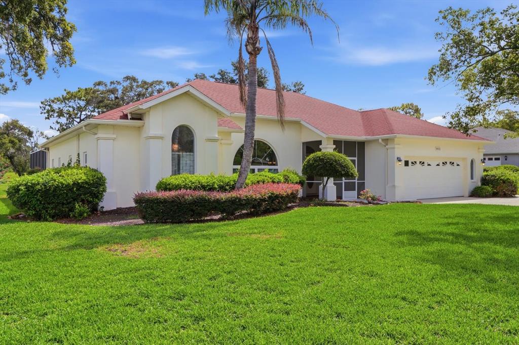 A single-story house with a red roof, cream-colored stucco walls, and a large front lawn — 9401 MERRIWEATHER DRIVE, WEEKI WACHEE, FL