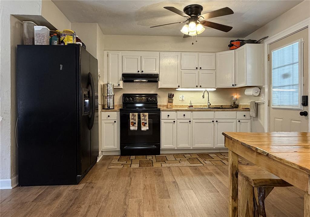 A kitchen features white cabinets, black appliances, wood-look flooring, and a wooden dining table — 18143 NW 251ST TERRACE, HIGH SPRINGS, FL