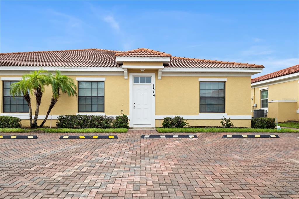 A yellow one-story building with a white front door and a brick-paved parking area — 1814 CORIANDER DRIVE, POINCIANA, FL