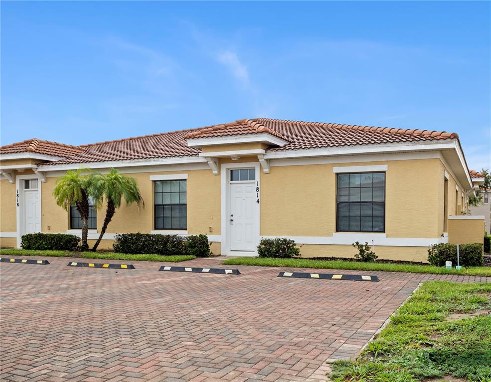 A single-story tan stucco building with a tiled roof and a brick-paved parking area — 1814 CORIANDER DRIVE, POINCIANA, FL