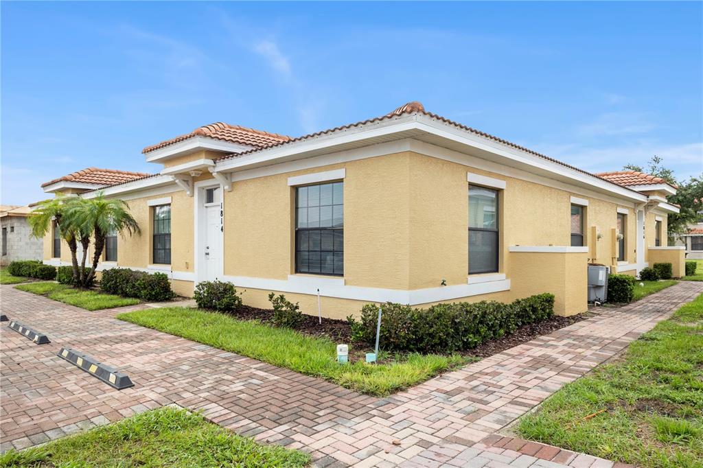 A single-story yellow stucco building with a tiled roof and a brick paver walkway — 1814 CORIANDER DRIVE, POINCIANA, FL