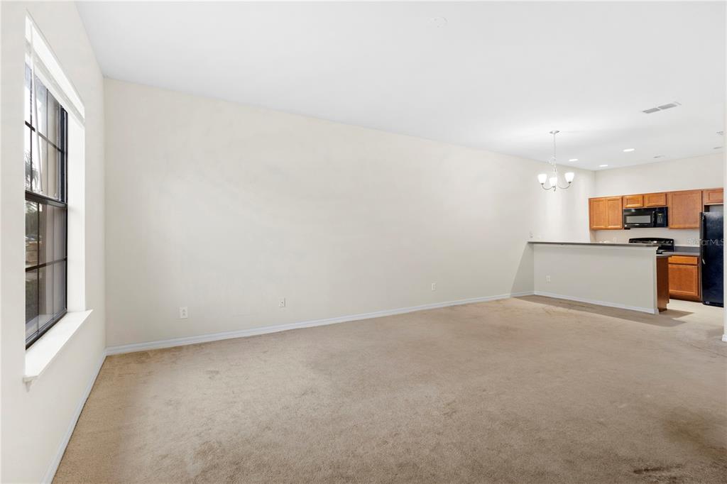 An empty living room with beige carpet and a breakfast bar opening to a kitchen — 1814 CORIANDER DRIVE, POINCIANA, FL