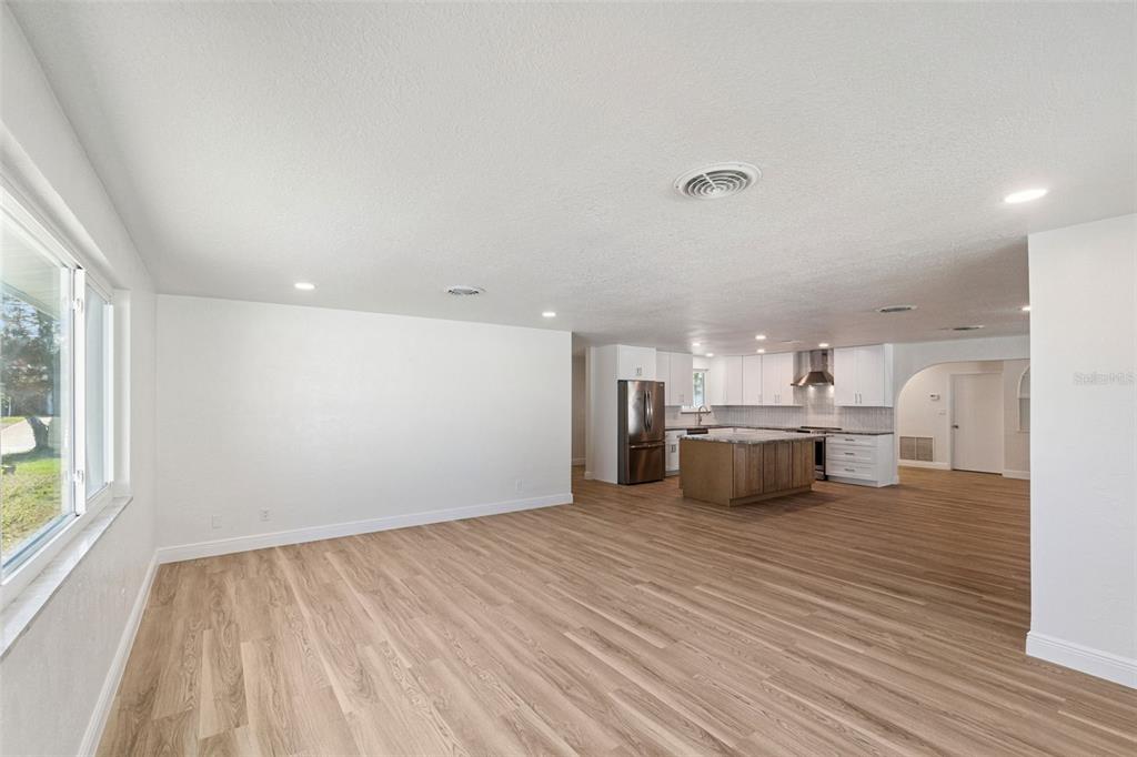 An open-concept living area features light wood-look flooring, white walls, and a modern kitchen — 3050 PRINCETON AVENUE, DAYTONA BEACH, FL