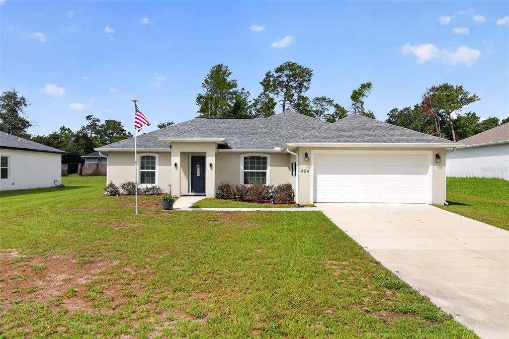 A single-story house with a beige exterior, a two-car garage, and an American flag — 484 MARION OAKS LANE, OCALA, FL