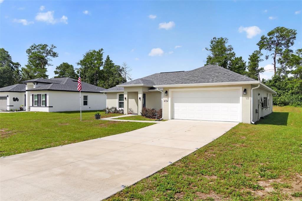 A single-story house with a white garage and a concrete driveway under a blue sky — 484 MARION OAKS LANE, OCALA, FL