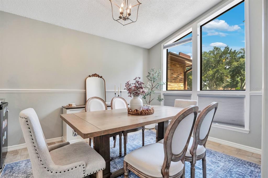 A dining room features a wooden table, upholstered chairs, a blue rug, and large windows — 3251 PINEWOOD COURT, KISSIMMEE, FL