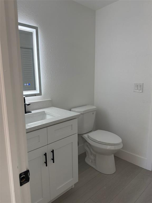 A bathroom features a white vanity with a lighted mirror, a toilet, and gray flooring — 2148 CATALINA DRIVE N, CLEARWATER, FL
