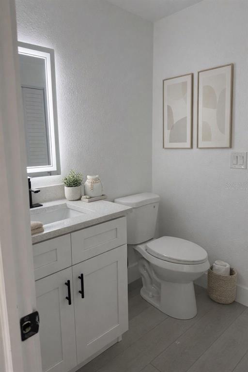 A bathroom features a white vanity, a lighted mirror, a toilet, and two framed wall prints — 2148 CATALINA DRIVE N, CLEARWATER, FL