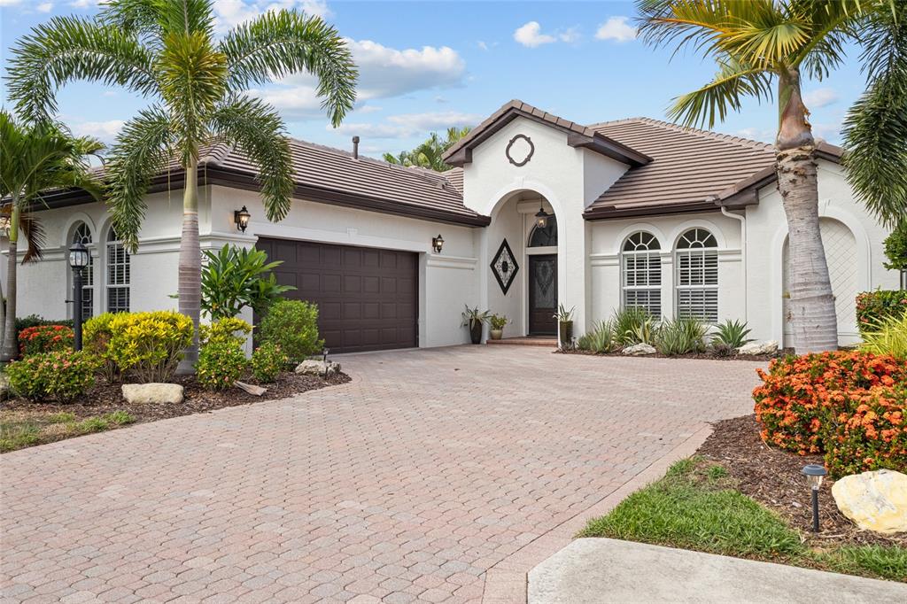 The exterior of a house features a brown garage door, arched entryway, and paver driveway — 7622 DESERT INN WAY, BRADENTON, FL