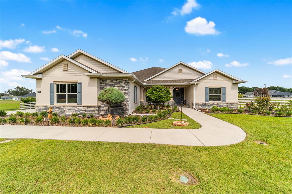 A single-story house with beige siding, stone accents, and a concrete walkway across the lawn — 1983 NW 79TH LOOP, OCALA, FL