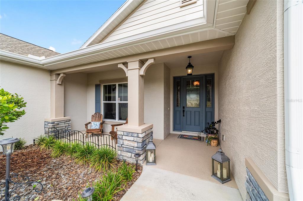 A covered front porch features a blue door, stone-based columns, and a small seating area — 1983 NW 79TH LOOP, OCALA, FL