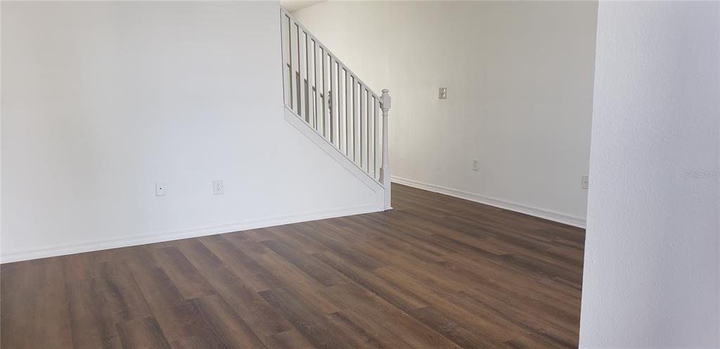 An empty room features wood-look flooring, white walls, and a staircase with a white railing — 6138 OLIVEDALE DRIVE, RIVERVIEW, FL