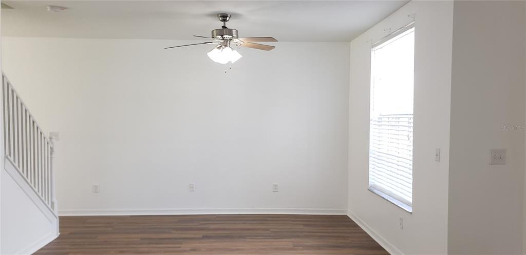 An empty room features white walls, wood-look flooring, a ceiling fan, and a staircase — 6138 OLIVEDALE DRIVE, RIVERVIEW, FL