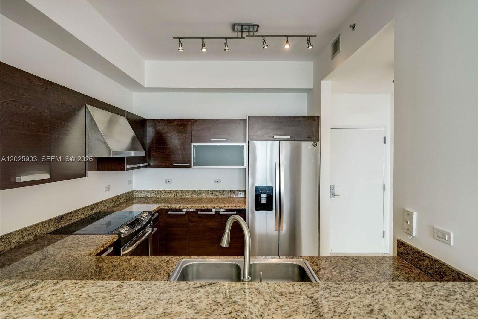 A kitchen features dark wood cabinetry, granite countertops, stainless steel appliances, and track lighting — 2525 SW 3rd Ave # 1009, Miami FL 33129, MIAMI, FL