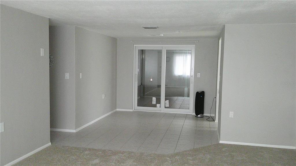 A room with light gray walls, carpeted flooring, and a tiled area leading to sliding doors — 1203 CHANCELLOR DRIVE, HOLIDAY, FL