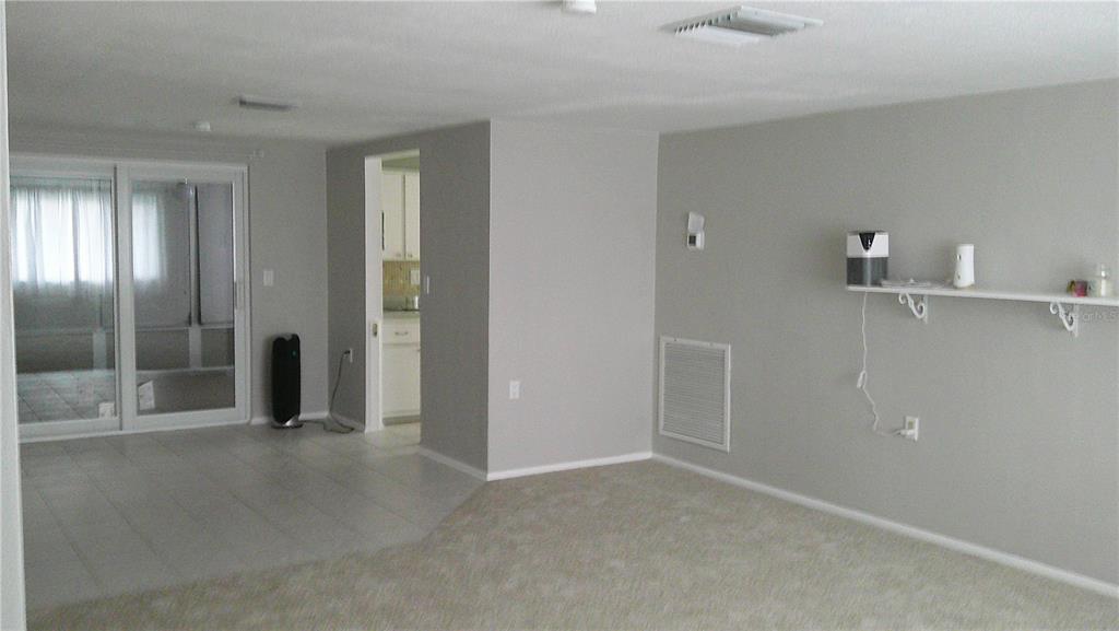 A living room with beige carpet, light gray walls, a white shelf, and a sliding door — 1203 CHANCELLOR DRIVE, HOLIDAY, FL